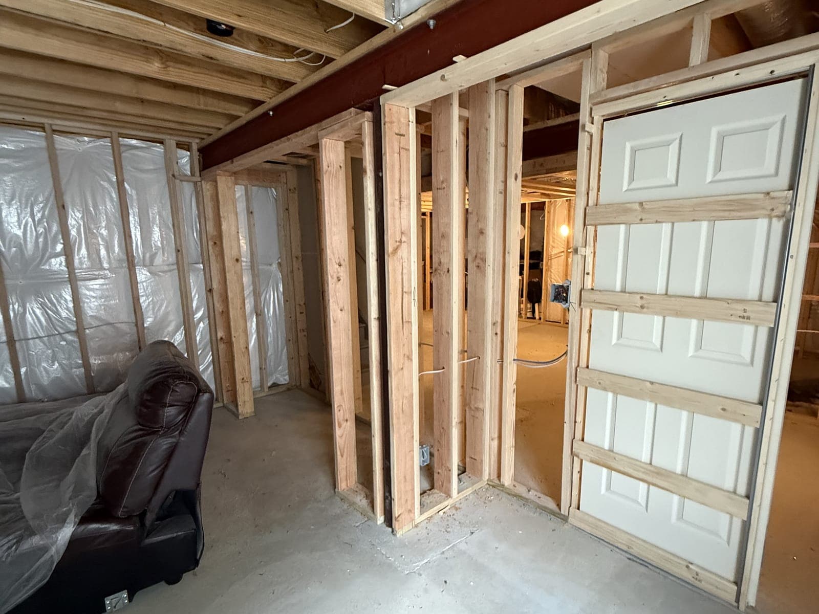 Basement framing under a steel beam: stud walls and doorways, and a six-panel door set in a pocket door frame at the right.