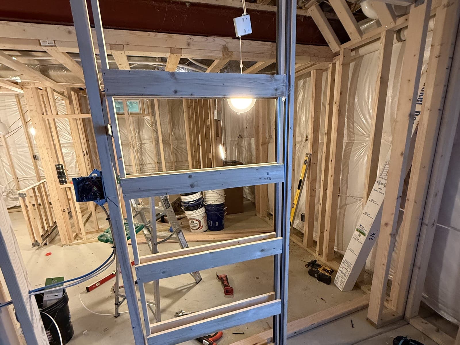 A pocket door frame set in a framed basement opening, the room beyond framed, with a ladder, buckets and tools on the slab.