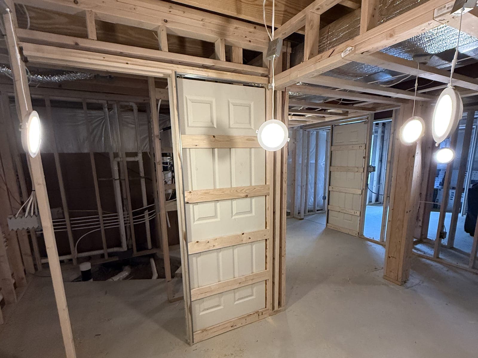 Two six-panel doors set in pocket door frames in basement framing, work lights hung from the joists.