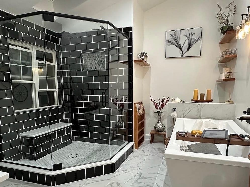 Shower with black subway tile and white grout, a hex tile floor and a glass enclosure, next to a freestanding tub.