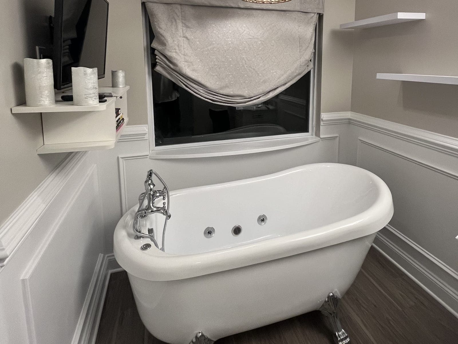 Clawfoot tub with chrome feet and faucet, picture-frame wainscoting, floating shelves and a wood-look plank floor.