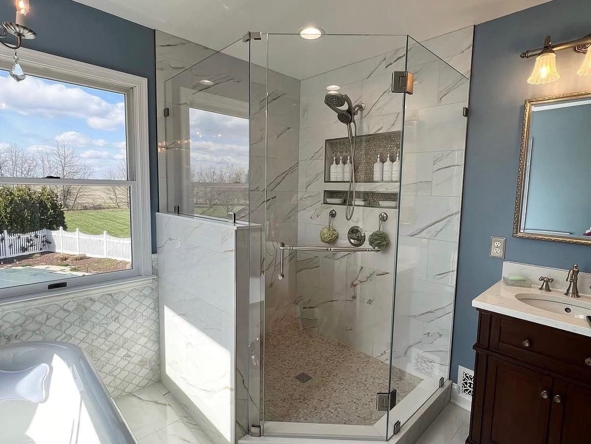 Corner shower with marble-look tile, a pebble floor and a glass enclosure, with a freestanding tub under the window.