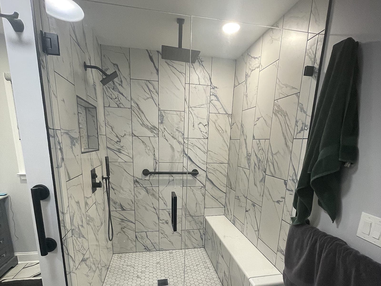 Walk-in shower with marble-look tile, matte black fixtures, a tiled bench, a hex tile floor and a frameless glass door.