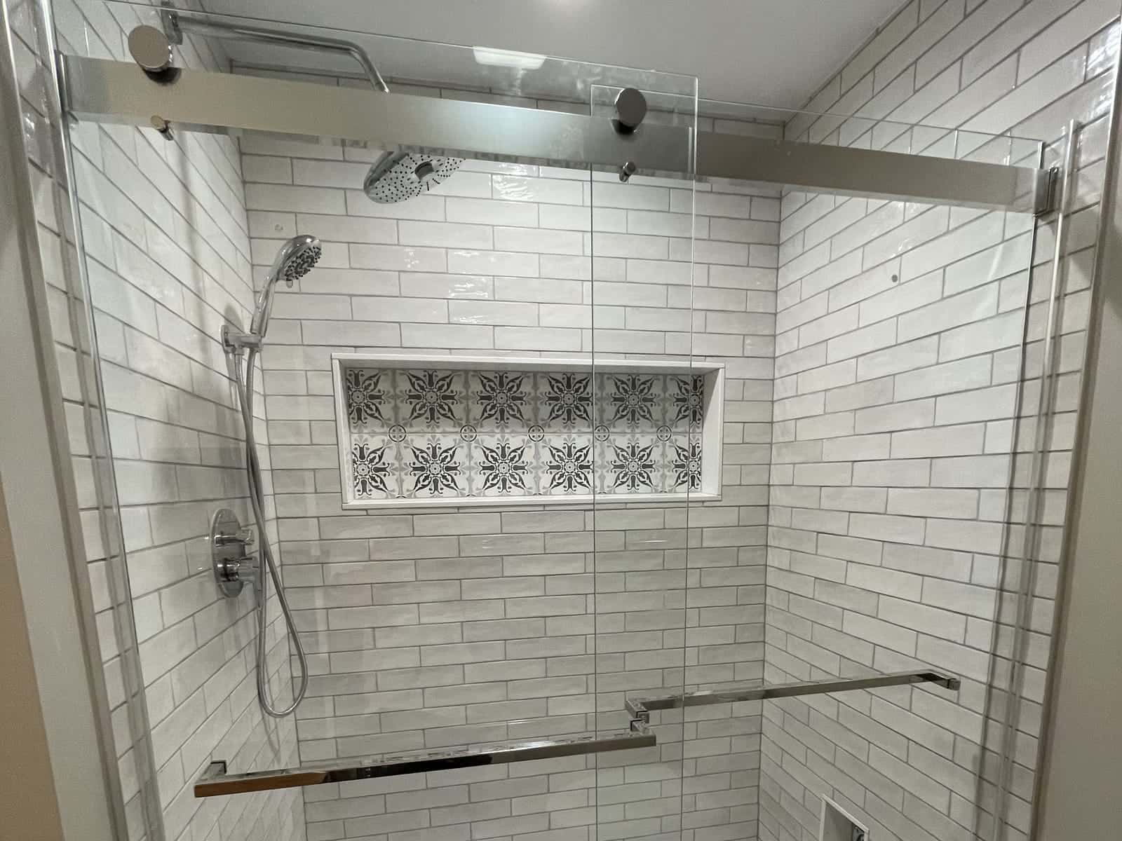 Walk-in shower with white subway tile, a patterned tile niche, a rain shower head and a sliding glass door.
