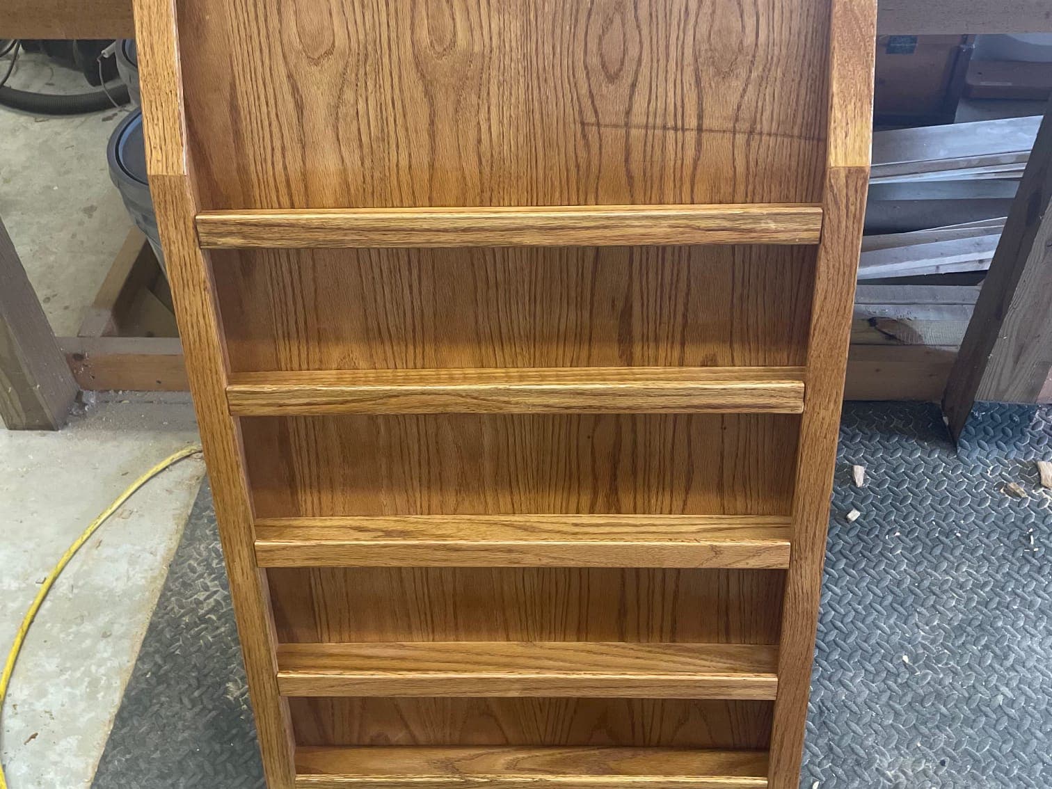 A stained oak wall rack with four rails, standing against a workbench on a shop floor.