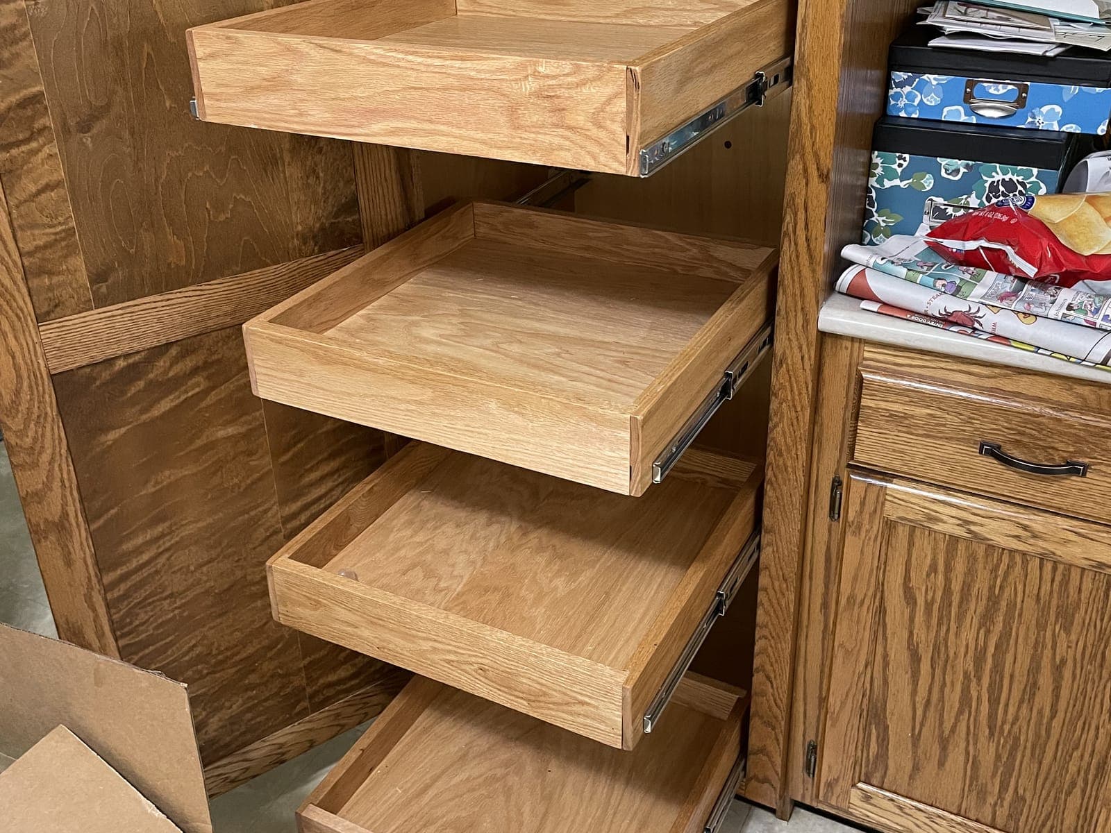 Four oak roll-out trays on full-extension slides, pulled out of a tall oak pantry cabinet beside oak base cabinets.