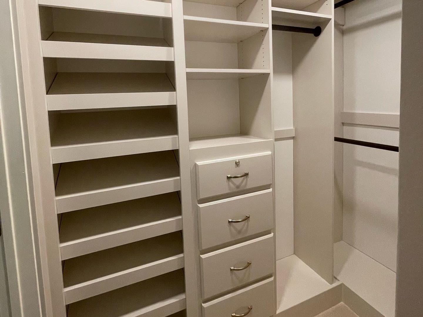 A walk-in closet wall with sloped shoe shelves, open cubbies, a bank of four drawers with brass pulls and a hanging rod.