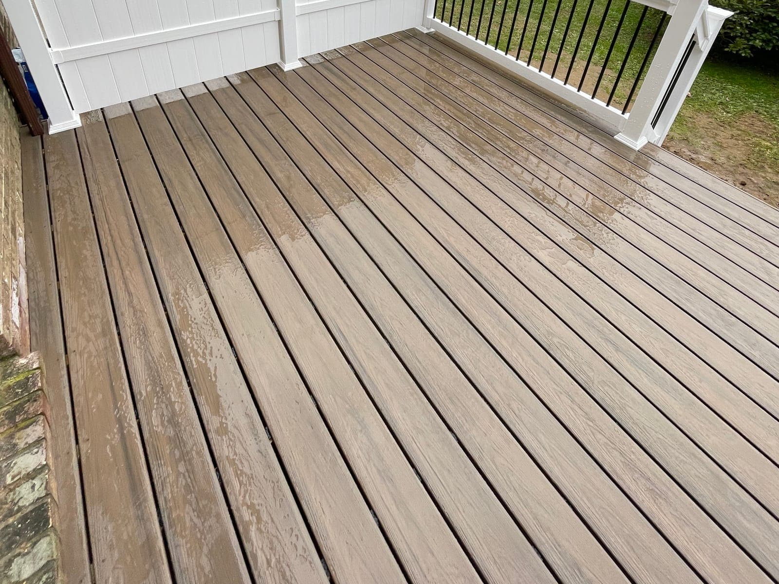 Composite deck boards running toward a white vinyl privacy fence, with a white rail and black balusters at the far edge.