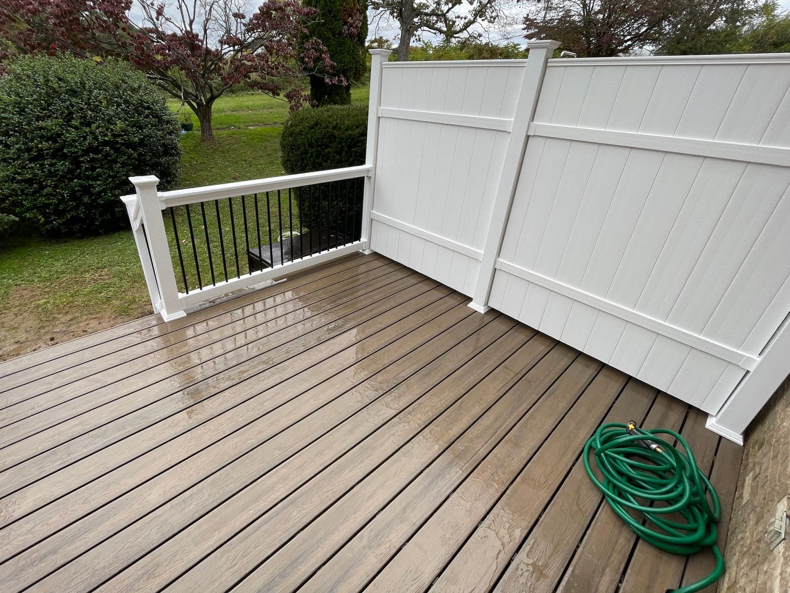 A composite deck with a white rail with black balusters and a white vinyl privacy fence, a garden hose coiled on the boards.