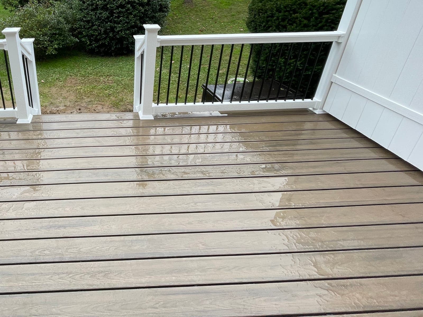 A composite deck with an opening in a white rail with black balusters, a white privacy fence at the right and a lawn beyond.