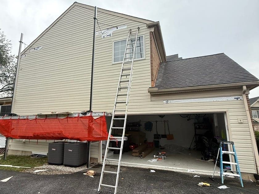 A garage gable end with new tan siding, a ladder still against it and the staging screen lowered.