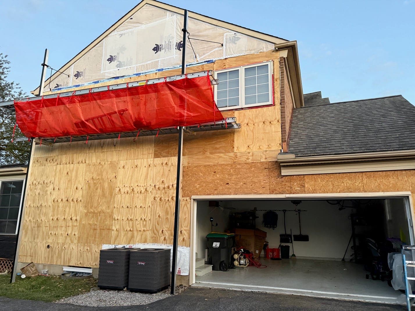 A garage gable end sheathed and wrapped with staging and an orange screen across it, before siding, the garage door open.